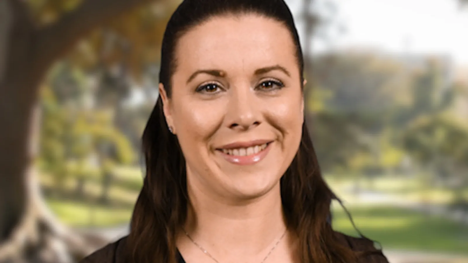 Image of a lady with brunette hair standing by a tree