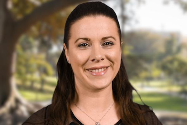 Image of a lady with brunette hair standing by a tree