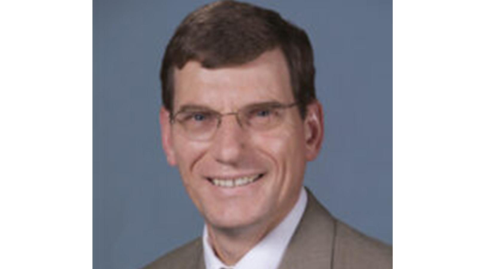 Smiling man with dark hair wearing a suit jacket and tie
