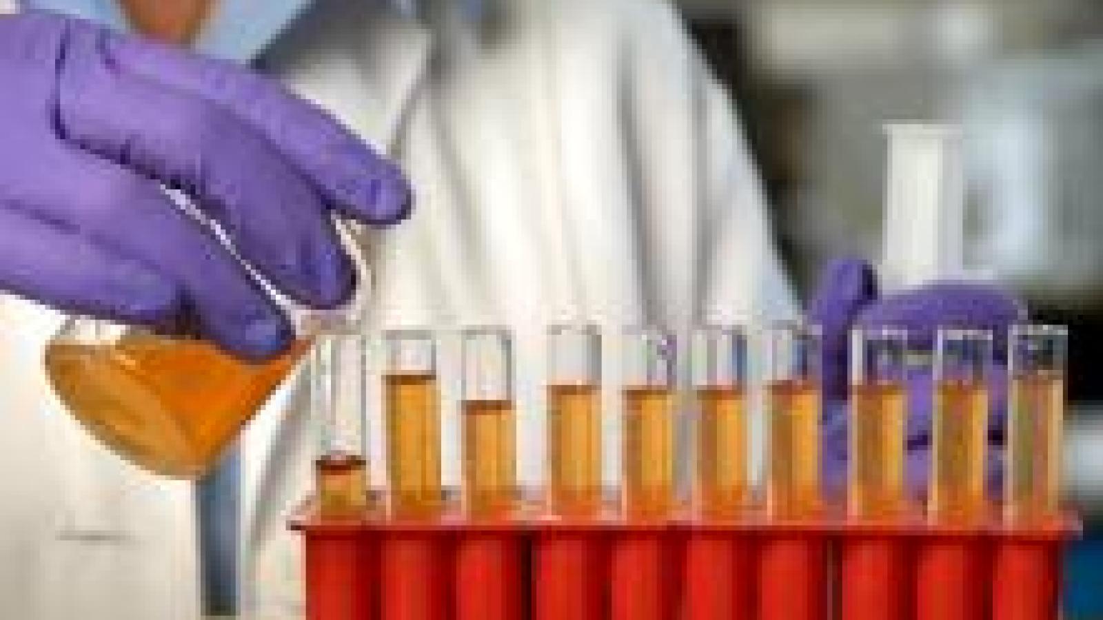 Person in lab coat pouring liquid into test tubes